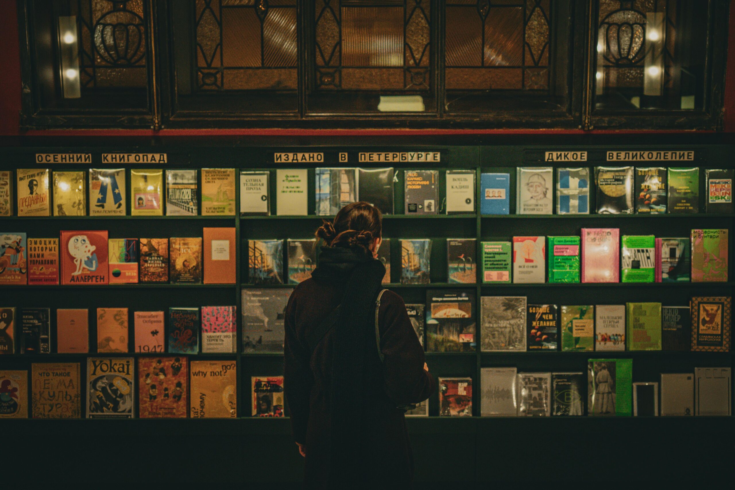 A woman selecting books from a well-lit shelf in a Saint Petersburg library.